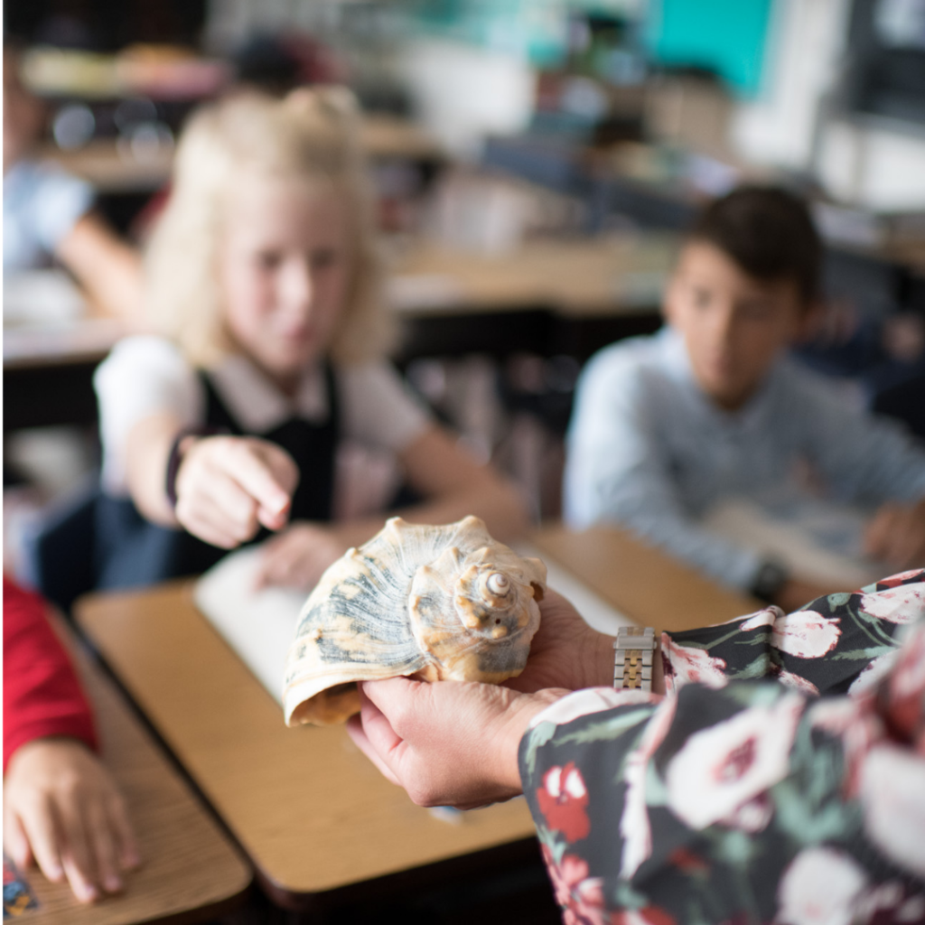A teacher holding a sea shell out to a student at Dayspring Christian Academy